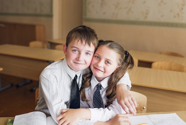 男の子と女の子の学生は机に座ってふける。男の子は女の子のおさげ髪を引っ張る。