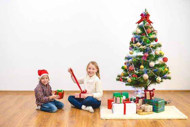 The boy and a girl unpack gift boxes near the christmas tree