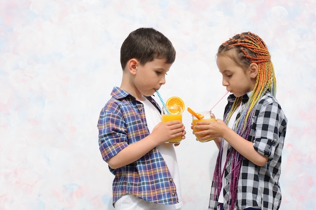 Boy and girl with braids drinking orange juice from glasses with a straw