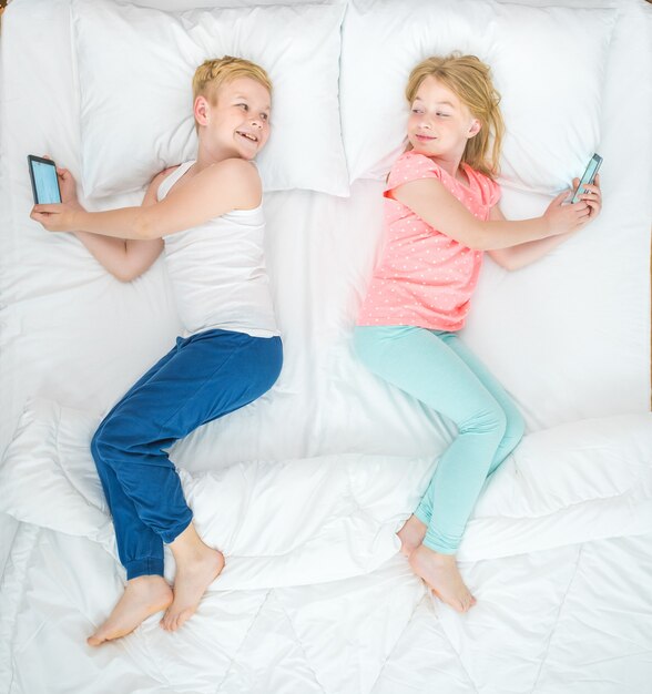 Photo the boy and girl with smartphones lay on the bed. view from above