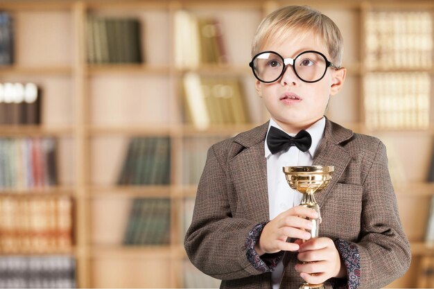 Boy in glasses holding trophy on background