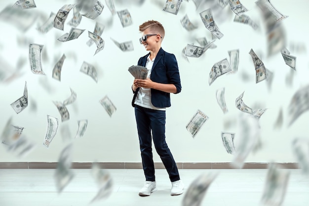 boy  glasses holds dollars and knows how to make money against the background of falling banknotes