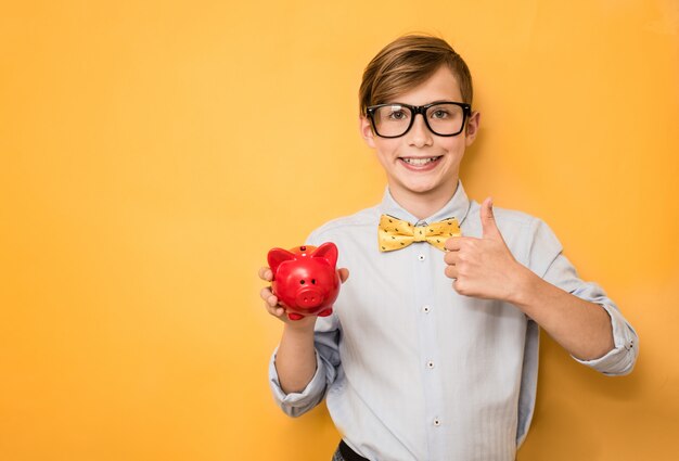 Boy in glasses with piggy bank against yellow