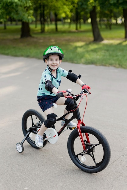 Boy in green helmet riding on his first bicycle in the summer park