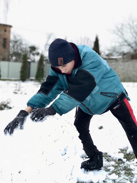 Foto un ragazzo con una giacca verde arrotola strati di neve su un pupazzo di neve in inverno