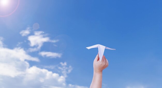 Photo boy hand holding a paper plane the background is a beautiful sky