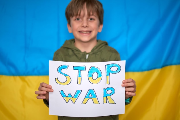 Foto mani del ragazzo che tengono banner di guerra di arresto disegnato su carta gialla blu sullo sfondo della bandiera ucraina