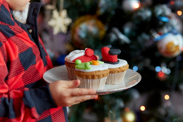 Boy hands holds decorative cupcakes in front of the Christmas tree Cozy Christmas time Good holidays mood Selective focus