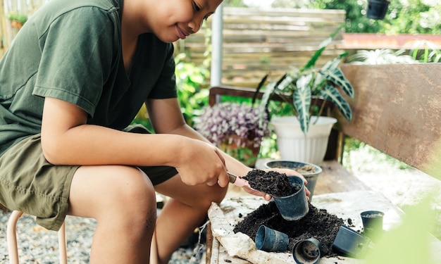 少年は、余暇活動のコンセプトを植えるための植物を準備するために、土を鉢にシャベルで入れる