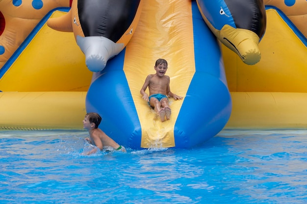 Мальчик прыгает в бассейн после спуска с водной горки летом Маленький мальчик скатывается с водной горки и веселится