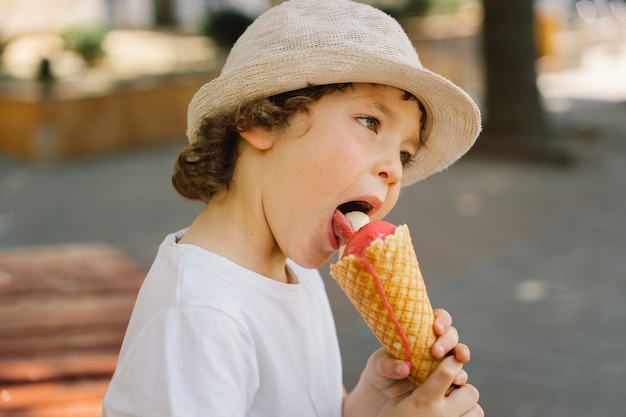 Boy in a hat is holding an ice cream and looks happy and surprised summer food and summer time