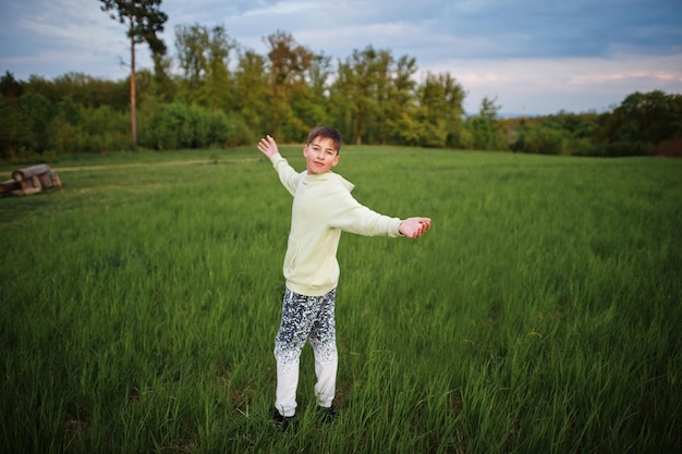 Мальчик веселится на лугу Подросток стоит в зеленой траве