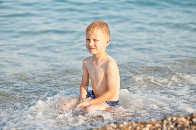 Boy having fun in sea or ocean waves in a summer sunny day.