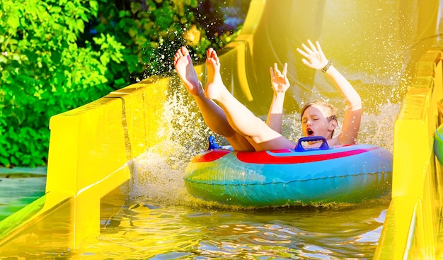 Boy having fun on yellow water slide in aquapark. Summer holiday.
