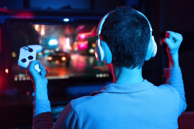 Photo boy in headphones plays a video online game on the big tv with neon lighting