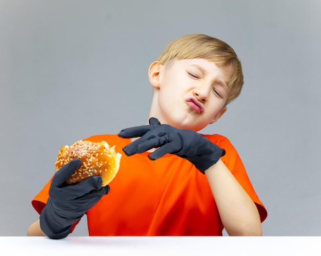 The boy held a bitten burger pushes it away from himself and demonstrates that he did not like the taste