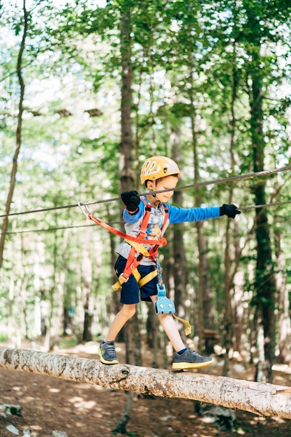 Boy in helmet walks on the wooden aerial trail in adventure park