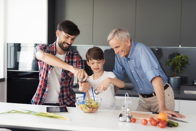 The boy and his father add spices to the almost ready salad.