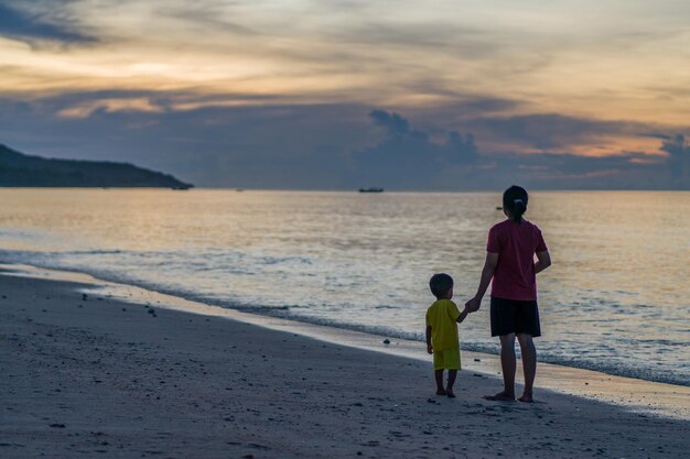 夕暮れの浜辺に立つ少年と母親。