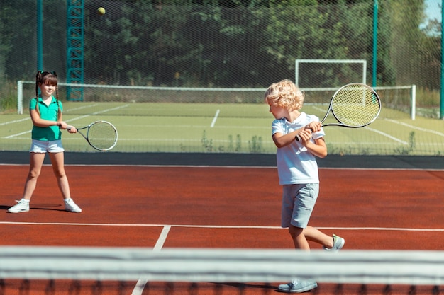 Photo boy hitting the tennis ball while playing with girl