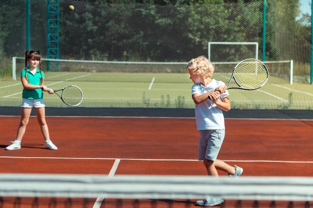 写真 女の子と遊んでいる間にテニスボールを打つ男の子