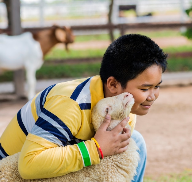 写真 少年は農場で羊を抱き、キスする。