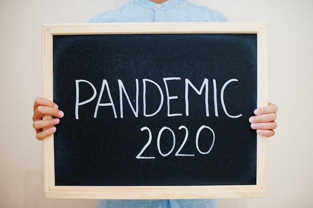 Boy hold inscription on the board with the text Pandemic 2020