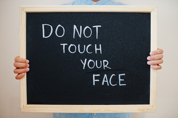 Boy hold inscription on the board with the text do not touch your face