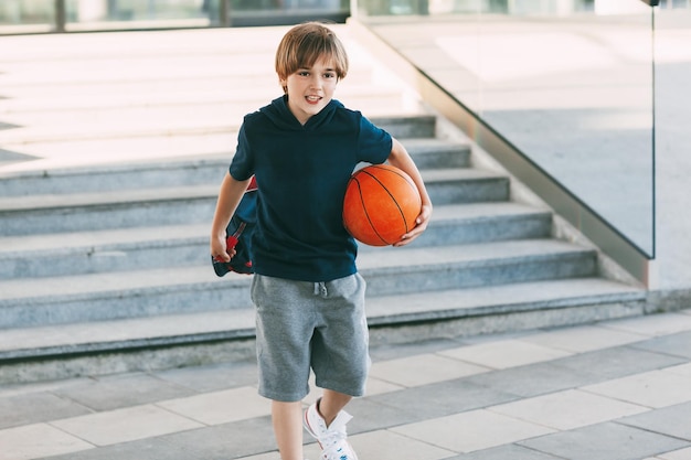 Photo boy holding basketball ball while walking on road