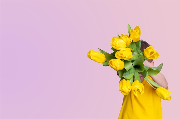 Boy holding a bouquet of yellow tulips on a pink background copy space top view Gift for mom Spring flowers