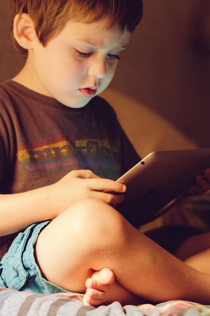 Boy holding digital tablet on bed at home