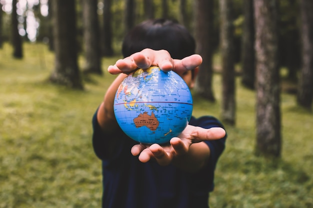 A boy holding earth globe with blurry forest