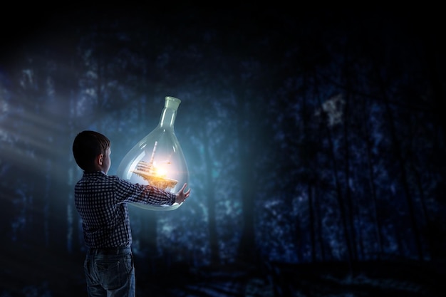 Boy holding flask with illuminated landscape in it. Mixed media