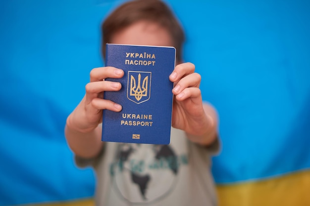 Boy holding in hands Ukrainian passport on yellowblue background Kids support Ukraine by showing heart on yellowblue flag Ukrainian crisis Russian aggression in Ukraine War of Russia against Ukraine