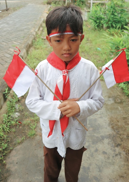 Photo boy holding indonesian flags while standing on field