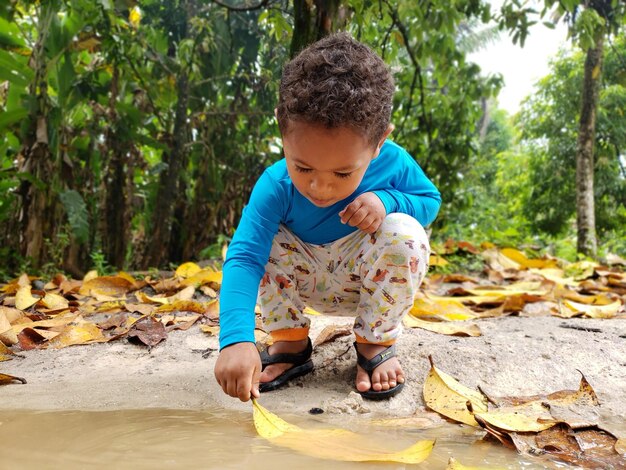 Photo boy holding leaf in lake at forest