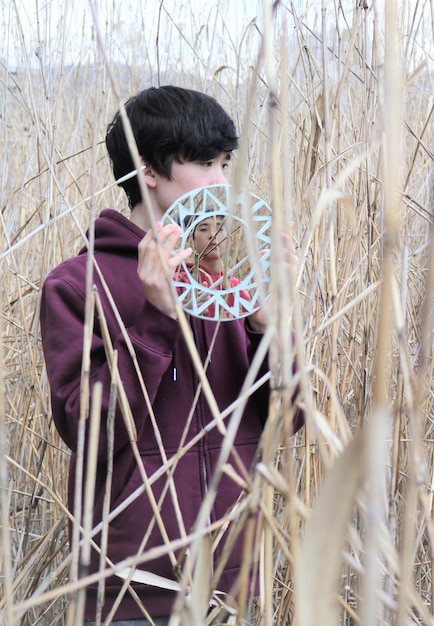 Photo boy holding mirror with friend reflection standing amidst plants on land