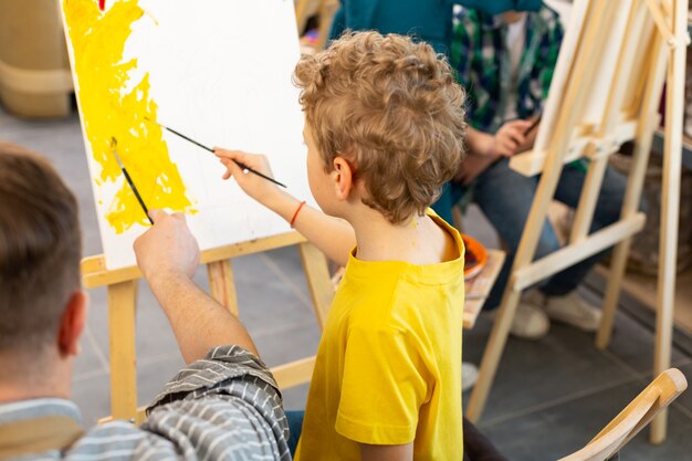 Boy holding painting brush coloring paper near teacher