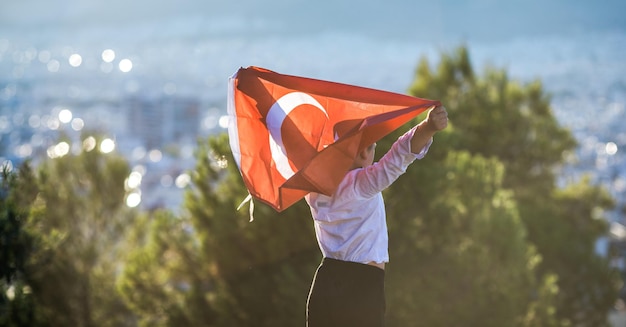 Boy holding Turkey flag against city Kid hand waving Turkish flag view from back copy space for text