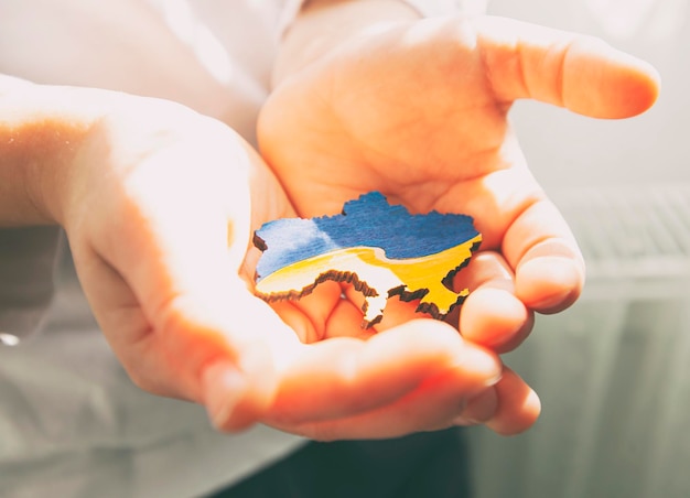 Photo boy holding wooden shape of ukraine colored in national colors in hand