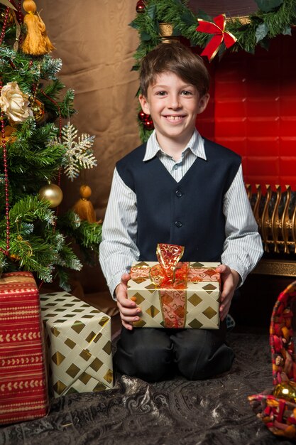 The boy holds a Christmas gift at the Christmas tree