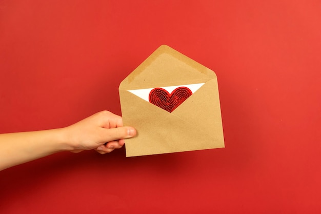 A boy holds an envelope with a love letter and red heart in it