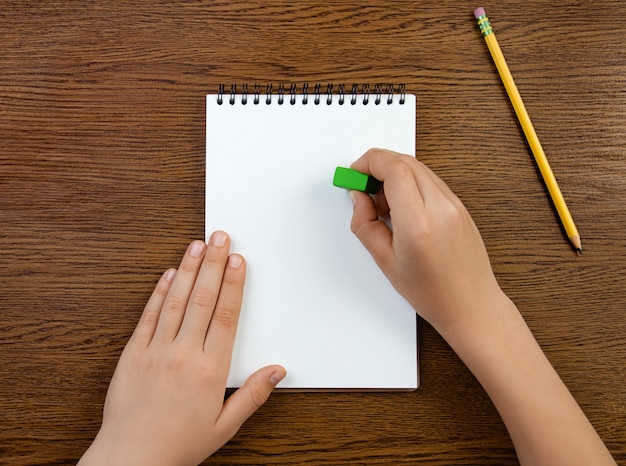 Boy holds the eraser and erases in white blank notebook