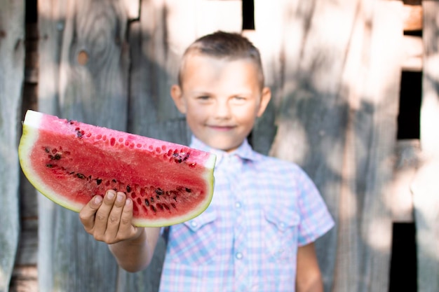 Boy holds a large piece of watermelon against a wooden rural wall