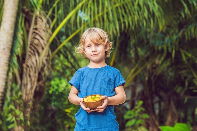 A boy holds a plate of mangoes on a background of palms