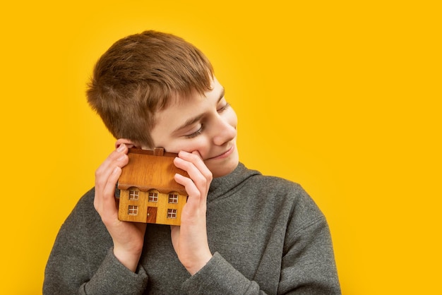 Boy holds small wooden house in his hands and hugs him Portrait of child with toy house on yellow background