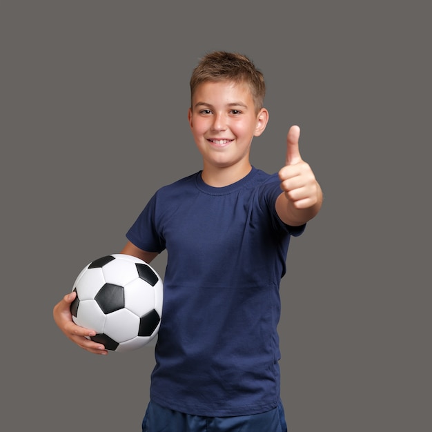 boy holds soccer ball and gesturing thumbs up