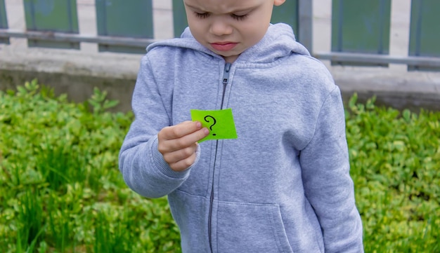 The boy holds stickers with a question mark on the background of the park Nature