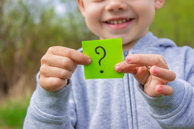 The boy holds stickers with a question mark on the background of the park Nature