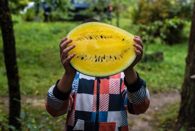 Photo a boy holds a yellow watermelon and wants to eat it